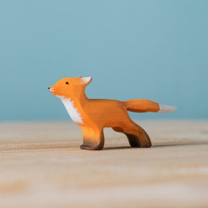 Single wooden fox toy with a white-tipped tail and chest, standing on a wood surface with a pale blue backdrop.