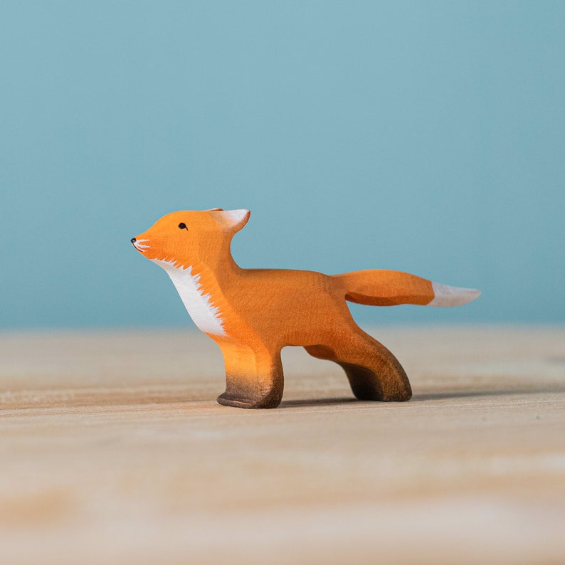 Single wooden fox toy with a white-tipped tail and chest, standing on a wood surface with a pale blue backdrop.