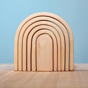 May include: A set of six wooden rainbow arch stacking toys. The arches are made of natural wood and are arranged in a graduated size, with the largest arch at the bottom and the smallest arch at the top.