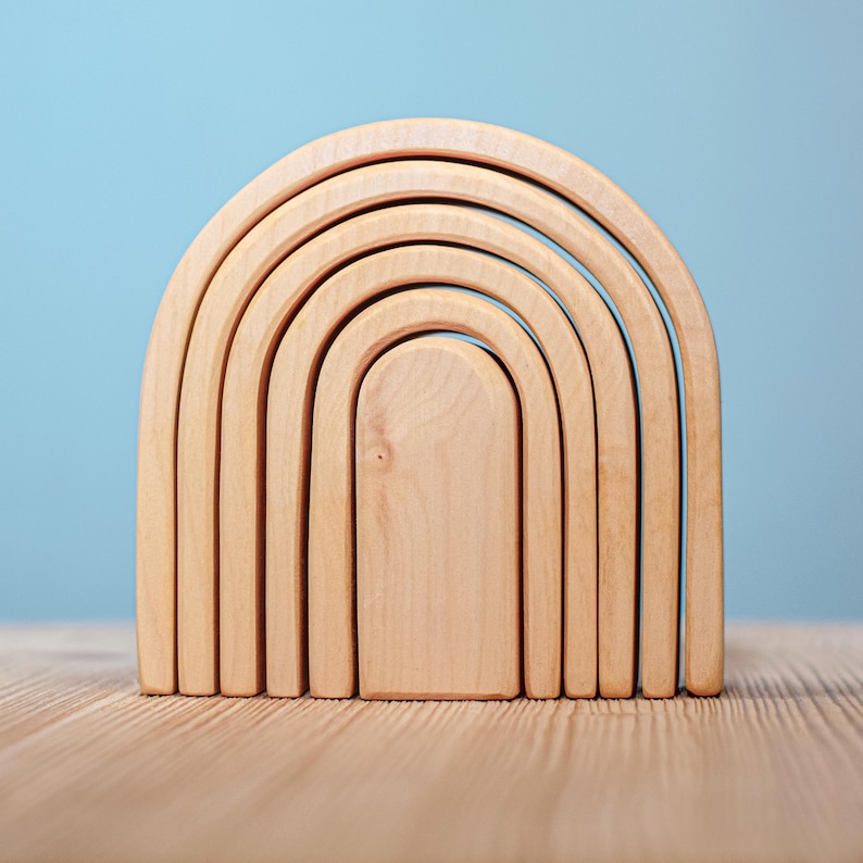 May include: A set of six wooden rainbow arch stacking toys. The arches are made of natural wood and are arranged in a graduated size, with the largest arch at the bottom and the smallest arch at the top.
