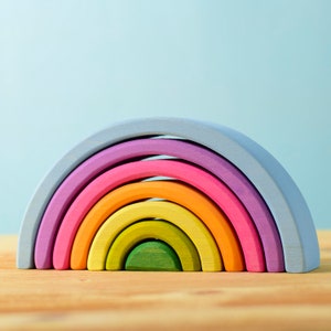 Könnte beinhalten: Ein regenbogenfarbenes Holz-Stapelspielzeug mit sieben Bögen in den Farben Blau, Lila, Rosa, Orange, Gelb, Grün und Hellgrün.
