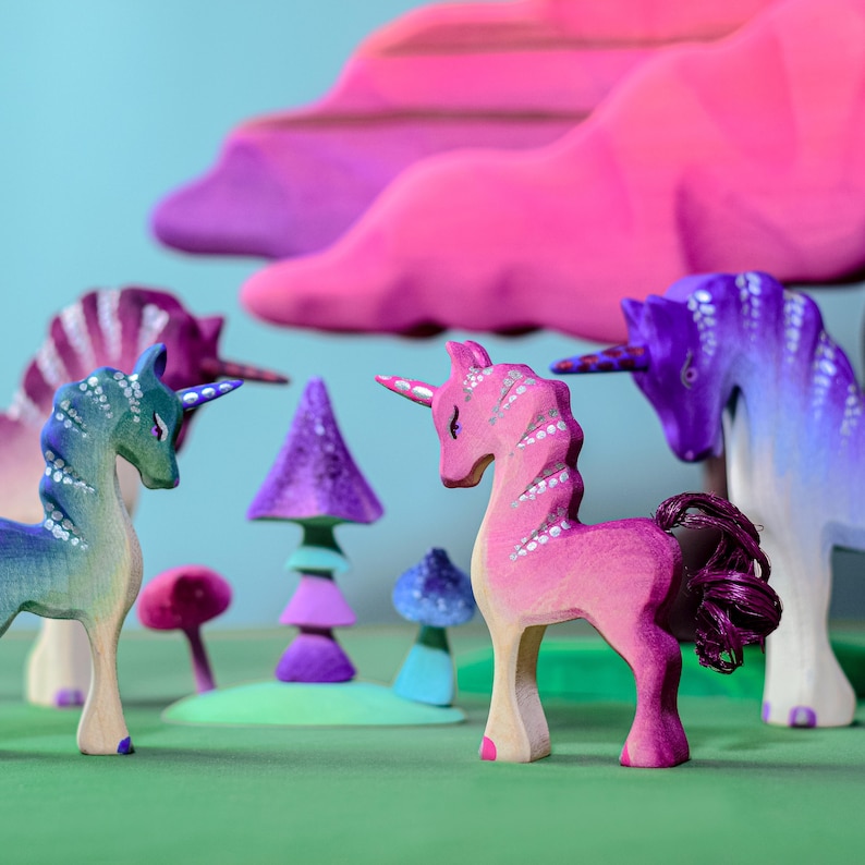 A group of colorful wooden unicorns standing in a field with mushrooms and clouds.