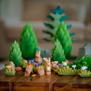 A whimsical wooden toy scene featuring various bunnies, a bird, and lush green trees on a wooden table.