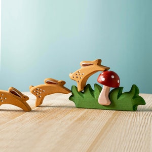 A red mushroom with white spots nestled in a green wooden grass base with three rabbits.