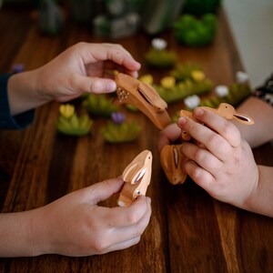 Children's hands playing with wooden animal toys, showcasing a bunny and a bird, amid a setting of wooden greenery.