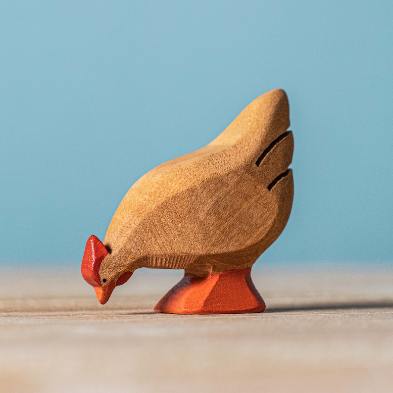 A beautifully crafted wooden rooster toy painted brown with black tail feathers, red comb, and orange feet, in a pecking position on a wooden surface.