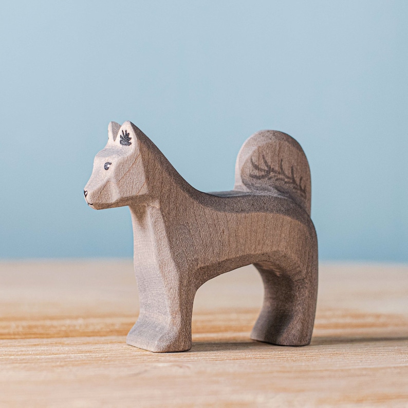 Artisanal wooden Shurik Dog toy with detailed leaf engravings in profile view, positioned on a wooden table against a tranquil blue backdrop, ideal for imaginative Montessori and Waldorf playtime