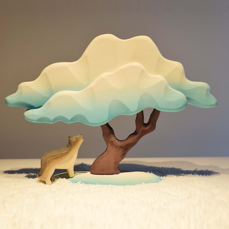 Wooden wolf figurine looking up at a pastel-colored tree on a white, snowy ground.