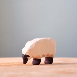 Small wooden sheep figure with black painted legs and face, standing on a wooden surface with a blue background.