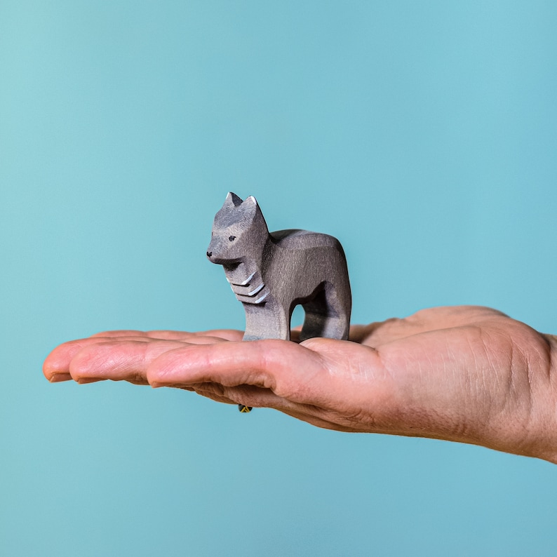 A handcrafted wolf statue in profile, standing alert on a smooth wooden surface, its details accentuated by the contrasting serene blue wall behind it.