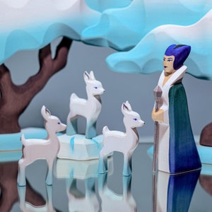 A wooden character with a purple head and green robe stands next to white deer on blue and white wooden ice pieces.