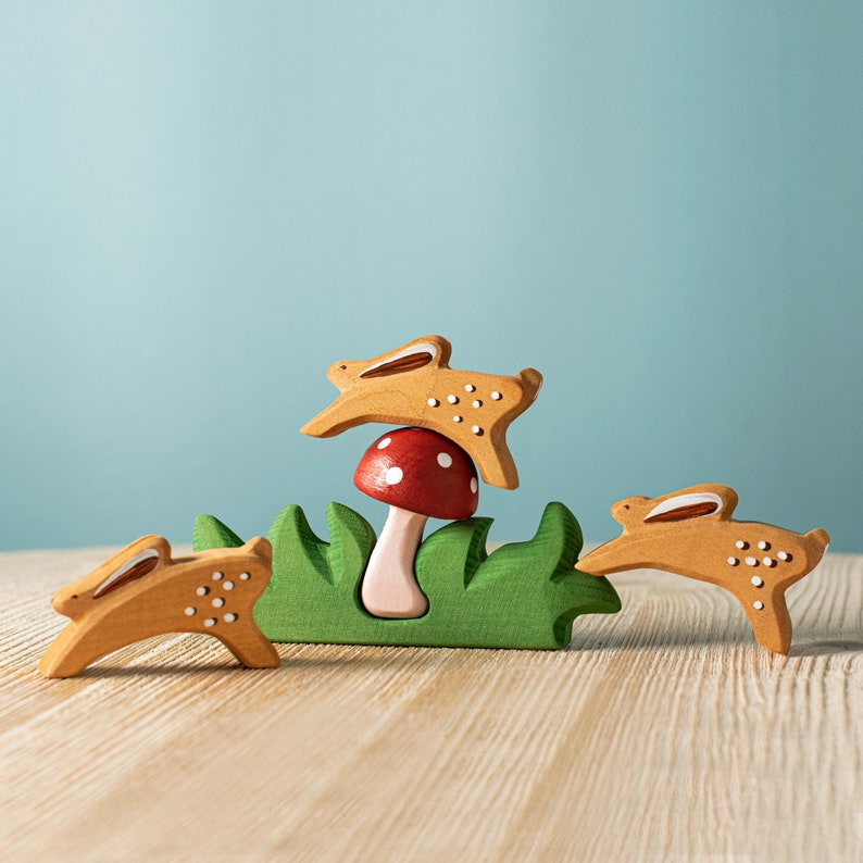 A red mushroom with white spots nestled in a green wooden grass base with three rabbits  around it on a wooden surface.