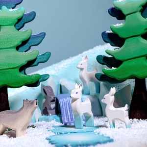 Wooden wolf figurine howling among a snowy forest scene with green pine trees and animal figurines.