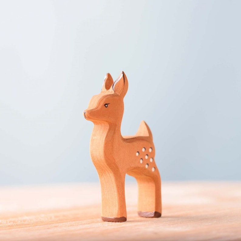 A wooden figurine of a deer with a simple, stylized design, standing on a smooth surface against a soft blue background makes for a unique handmade gift.