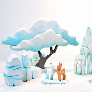 White wooden animal figures on pale blue wooden icebergs with a white tree and background, resembling a winter scene.