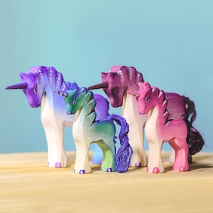 Four handcrafted wooden unicorns in various colors, sitting on a wooden table.