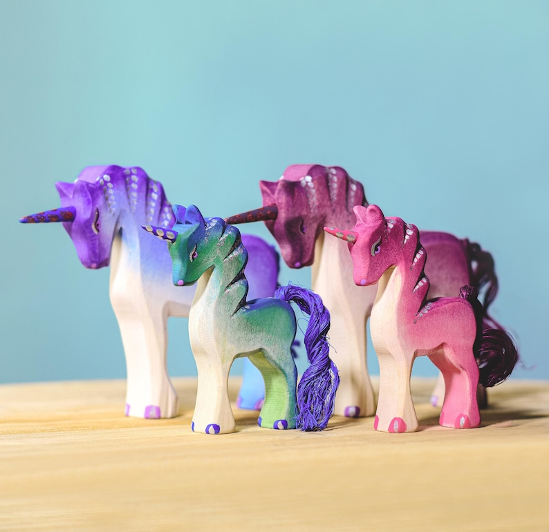 Four handcrafted wooden unicorns in various colors, sitting on a wooden table.