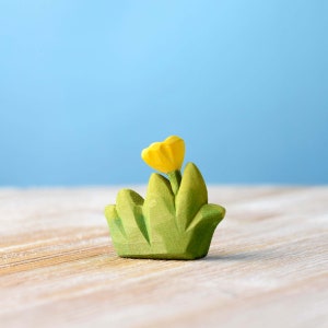 Close-up of a hand-painted wooden bush with a bright yellow flower against a soft blue background.