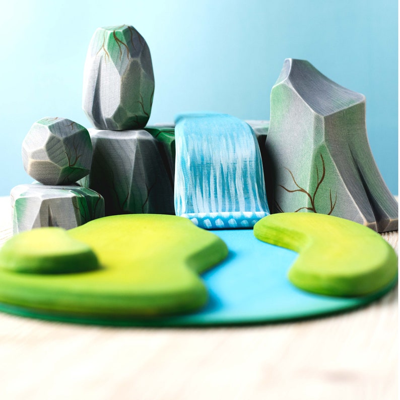 Hand-painted wooden toy set mimicking a natural landscape with textured mountains, cascading waterfall, and vibrant green islands.