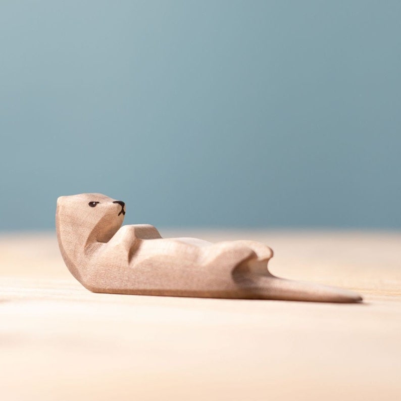 Artistic wooden otter figurine lying on its back in a relaxed posture, showcasing the craftsmanship of Waldorf-inspired toys.