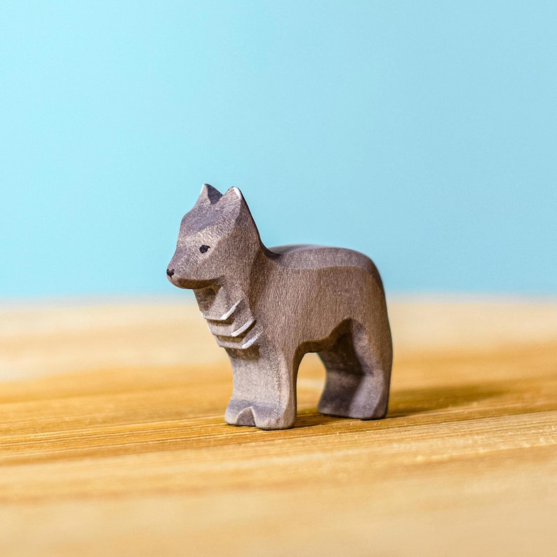 Wooden toy wolf with detailed carvings and visible wood layers, standing on all fours on a wooden table, with a soft blue background.