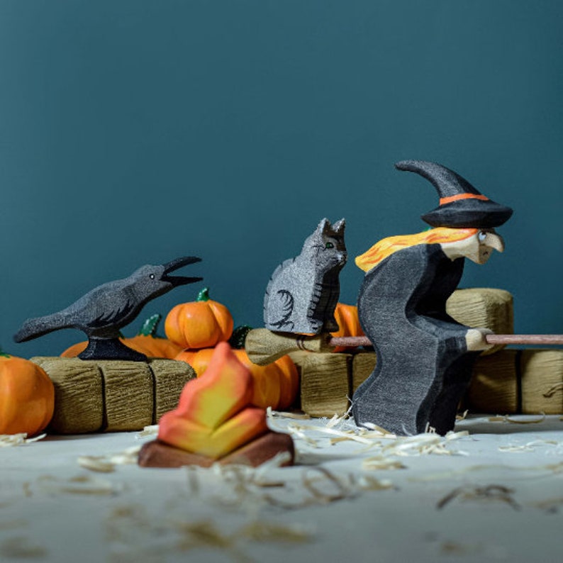 Wooden cat figure featured in a whimsical Halloween setting with a witch, crow, and pumpkins, illustrating a festive storytelling scene.