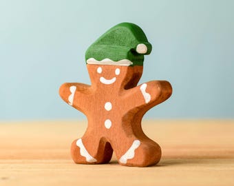 May include: A wooden gingerbread man figurine with a green hat and white icing details. The figurine has a smiling face and is standing on a wooden surface.