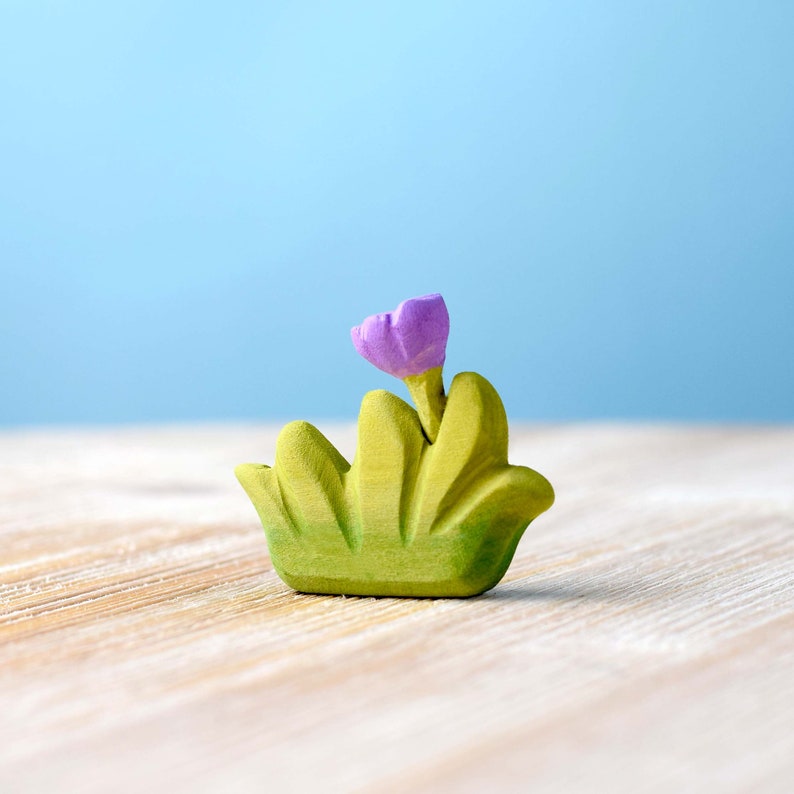 Handcrafted wooden bush with a single purple flower, painted in green and set against a blue backdrop.