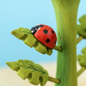 A red wooden ladybug toy perched on a bright green wooden leaf against a sky-blue background.