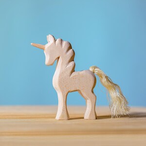 Wooden unicorn with a spiral horn and wavy tail, placed on a light wooden surface with a sky-blue background.