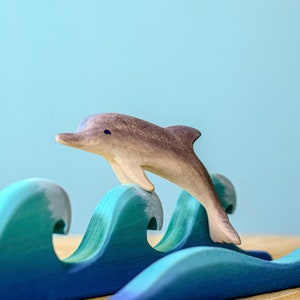 This wooden dolphin by BumbuToys glides over a cresting blue wave, illustrating the fluidity and dynamic nature of aquatic play in a tranquil oceanic scene.
