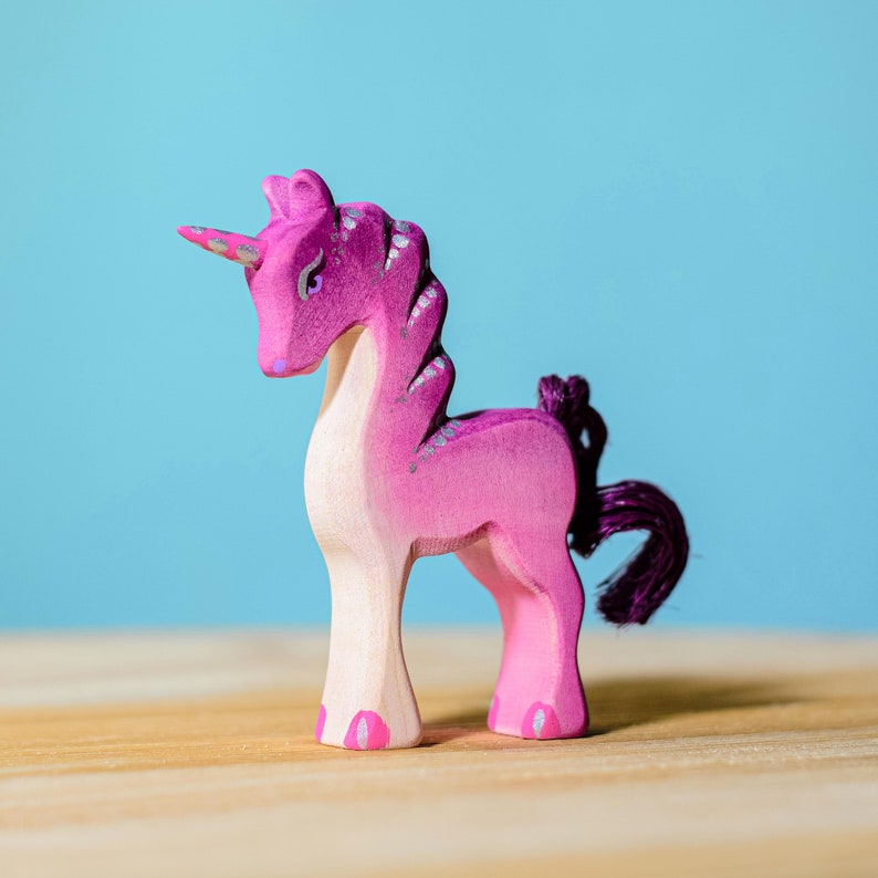 Pink wooden unicorn figurine sitting on a tabletop.