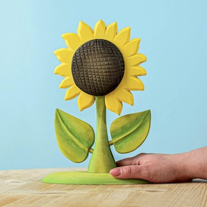 Sustainable wooden sunflower toy with detailed petals and leaves on a wooden surface with soft blue backdrop