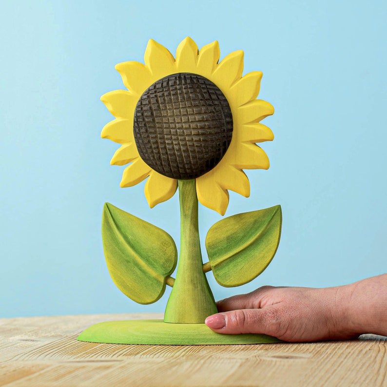 Sustainable wooden sunflower toy with detailed petals and leaves on a wooden surface with soft blue backdrop