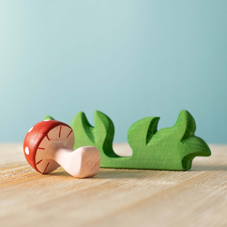 Wooden mushroom toy tipped over on its side with a detailed gill pattern, beside a green grass base, on a wooden surface.