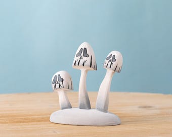 May include: A whimsical wooden sculpture featuring three white mushrooms with gray and black facial details. The mushrooms are attached to a white base, creating a unique decorative piece. The background is a light blue.