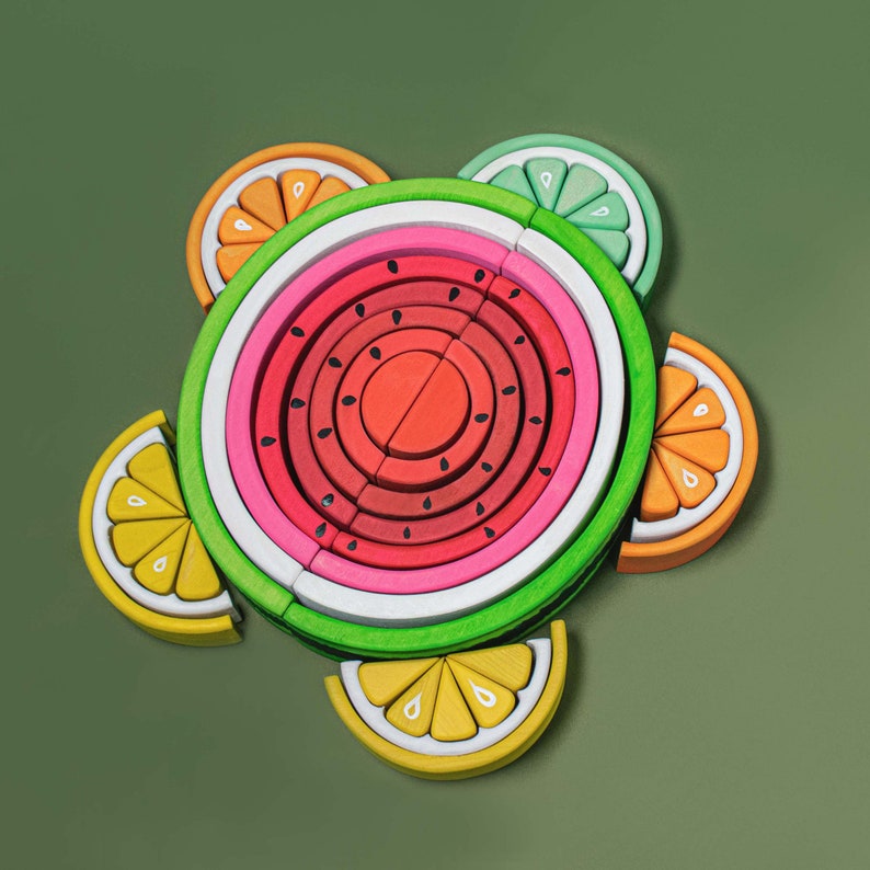 Set of Montessori-inspired wooden stacking toys including watermelon on a green background.