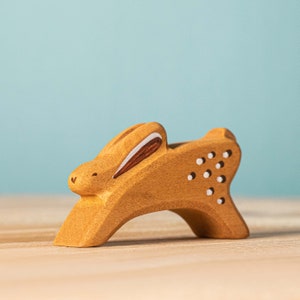 A wooden toy bunny with decorative cut-outs sitting on a flat surface against a soft blue background. This item makes for a perfect handmade gift.