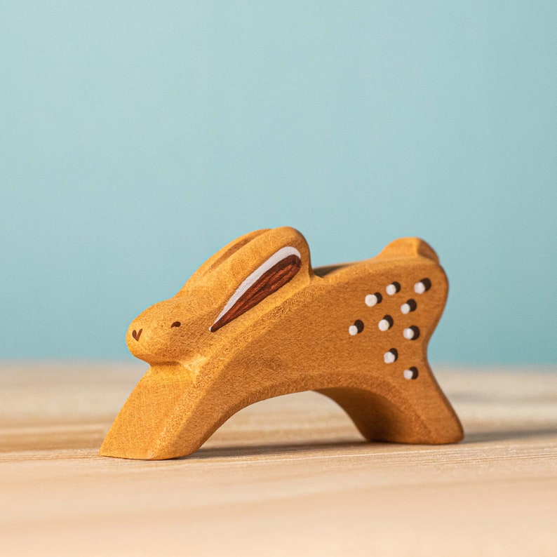 A wooden toy bunny with decorative cut-outs sitting on a flat surface against a soft blue background. This item makes for a perfect handmade gift.