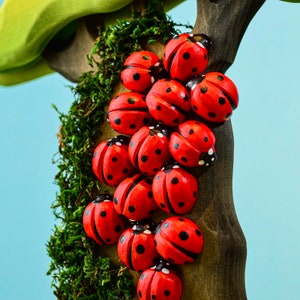 A vibrant group of red wooden ladybugs climbing up a tree trunk against a pastel blue background, creating a playful scene.