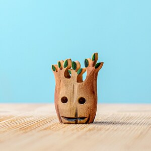 A small wooden tree stump with whimsical face carving and green foliage details standing on a wooden table with a soft blue background.