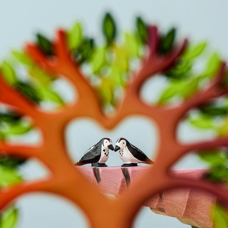 Two wooden bird figurines framed by the branches of a handcrafted wooden heart tree toy, capturing a moment of connection