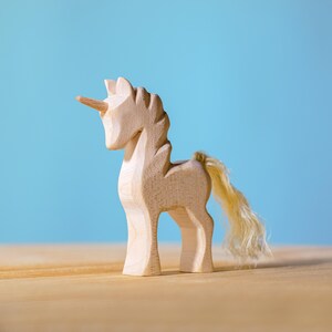 A single wooden unicorn figure with flowing mane and prominent horn, standing on a wooden table with a clear blue backdrop.