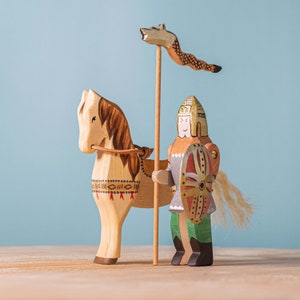 Side view of a wooden knight on horseback, with a lance flying a fox banner, showcasing traditional painting details against a calming blue backdrop.