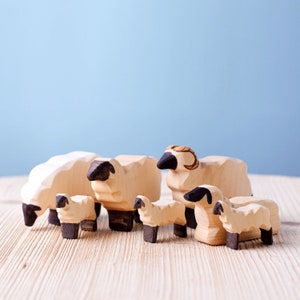 A family of wooden sheep toys in various sizes on a wooden surface, with the largest sheep featuring a detailed curled horn.