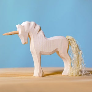 Wooden unicorn toy facing left with a pronounced horn and textured mane, displayed on a wooden surface against a light blue background.