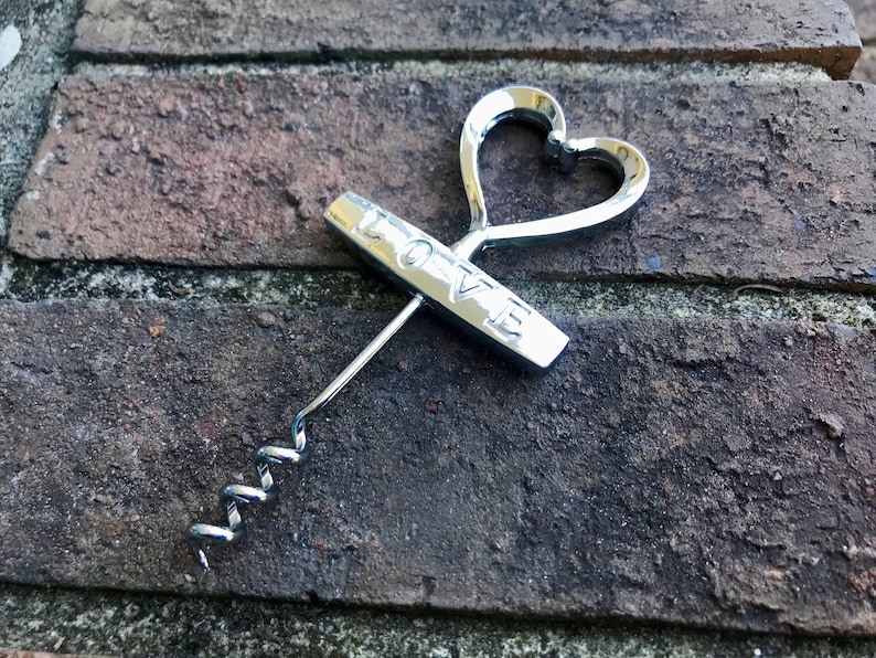 May include: Silver-toned heart-shaped bottle opener with a corkscrew and the word "LOVE" engraved on the handle.