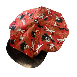 May include: A red and black patterned newsboy cap with a skull and crossbones design. The cap has a black leather brim.