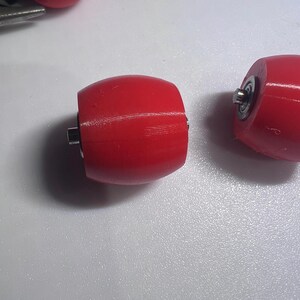 Puede incluir: Tres ruedas de color rojo brillante en forma de barril con l&iacute;neas de textura impresas en 3D visibles. Cada rueda cuenta con un inserto de rodamiento de bolas de metal central que sobresale del lado, dise&ntilde;ado para una rotaci&oacute;n suave.