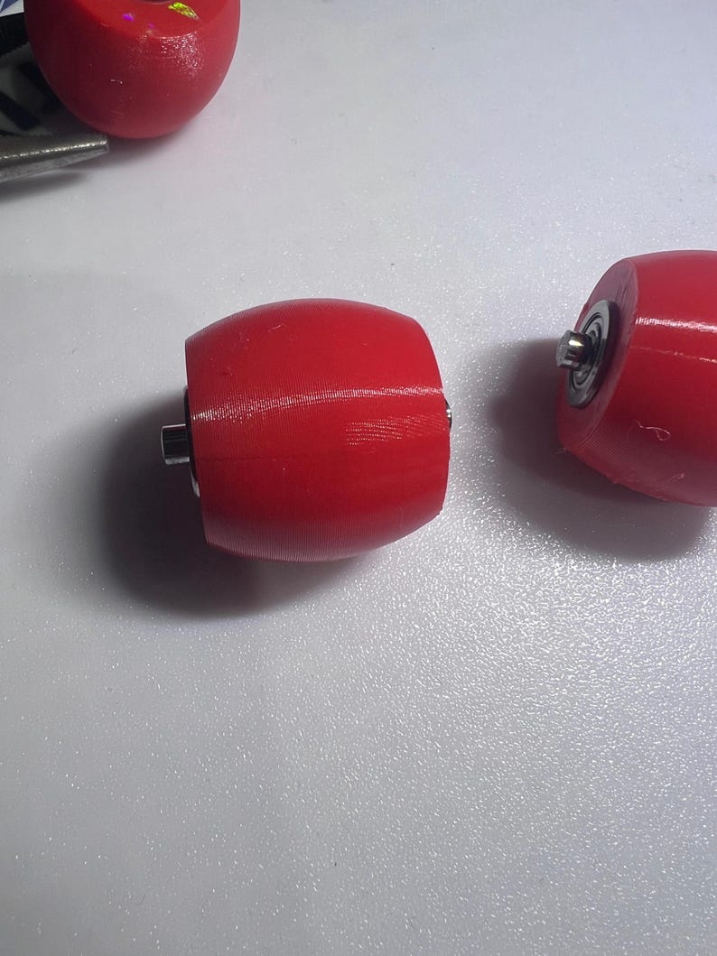 Puede incluir: Tres ruedas de color rojo brillante en forma de barril con l&iacute;neas de textura impresas en 3D visibles. Cada rueda cuenta con un inserto de rodamiento de bolas de metal central que sobresale del lado, dise&ntilde;ado para una rotaci&oacute;n suave.